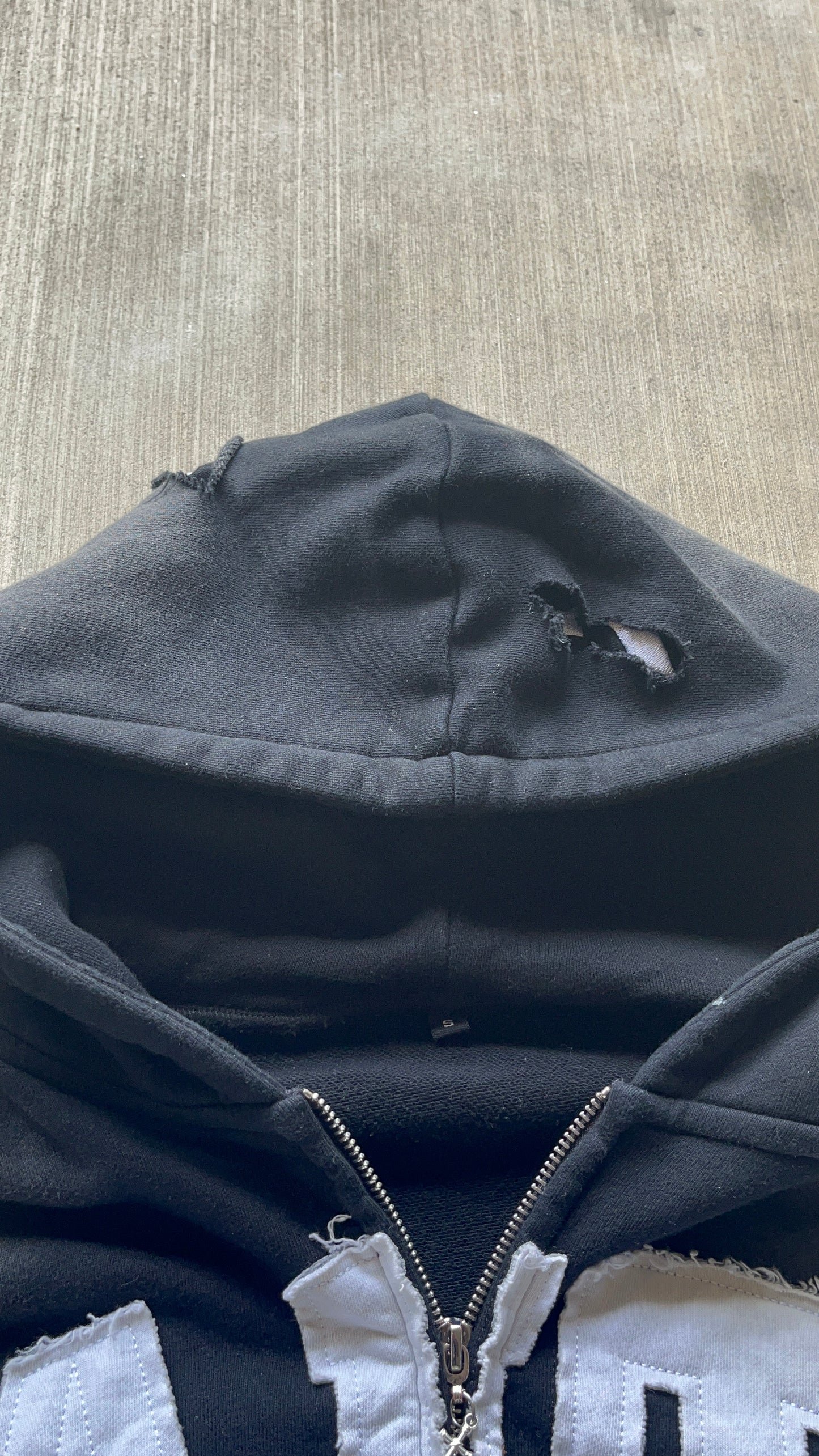 Black distressed zip-up hoodie with unique cuts, frayed cropped fit, and trendy sun wash for a stylish, worn-in look